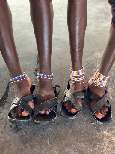 Zwei Paare Füße in Sandalen mit bunten Armbändern um die Knöchel.