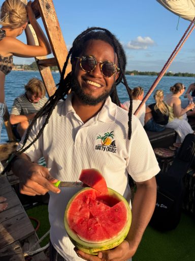 Lächelnder Mann mit Sonnenbrille schneidet eine Wassermelone auf einem Boot.