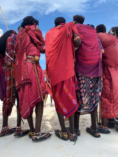 Gruppierung von Menschen in traditionellen roten Gewändern, Rückenansicht vor blauem Himmel.