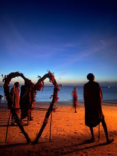 Silhouetten von Menschen am Strand vor einem herzförmigen Dekor bei Dämmerung.