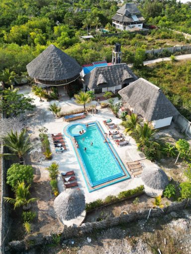 Landschaft mit offenem Pool, Liegen und mehreren Gartenhäuschen umgeben von Pflanzen.