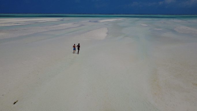 Zwei Personen wandern über einen weiten, sandigen Strand bei klarem, blauem Himmel.