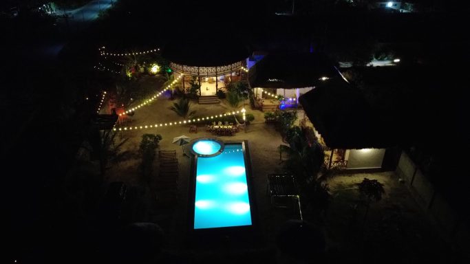 Beleuchteter Außenbereich mit Pool und Entspannungsbereichen bei Nacht.
