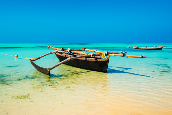 Fischerboot im flachen, türkisfarbenen Wasser unter klarem blauem Himmel.