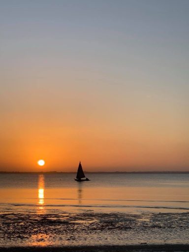 Sonnenuntergang über dem Meer mit einem Segelboot in der Silhouette.
