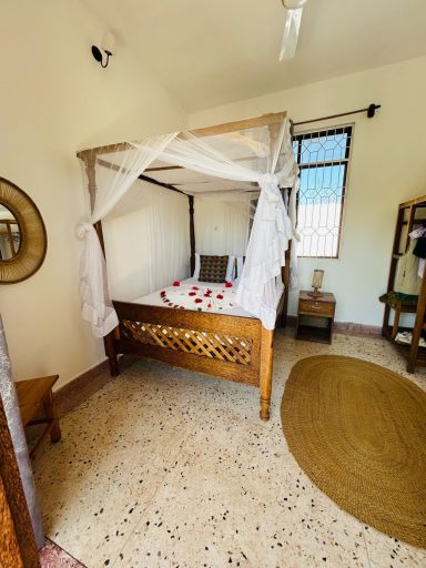 Helles Schlafzimmer mit einem Baldachinbett und roten Blüten auf der Bettdecke.