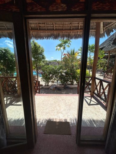 Blick von einer offenen Tür auf einen Garten mit Pool und exotischen Pflanzen.