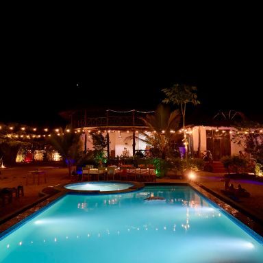 Poolbereich mit Lichtern und Palmen, umgeben von einem Garten bei Nacht.